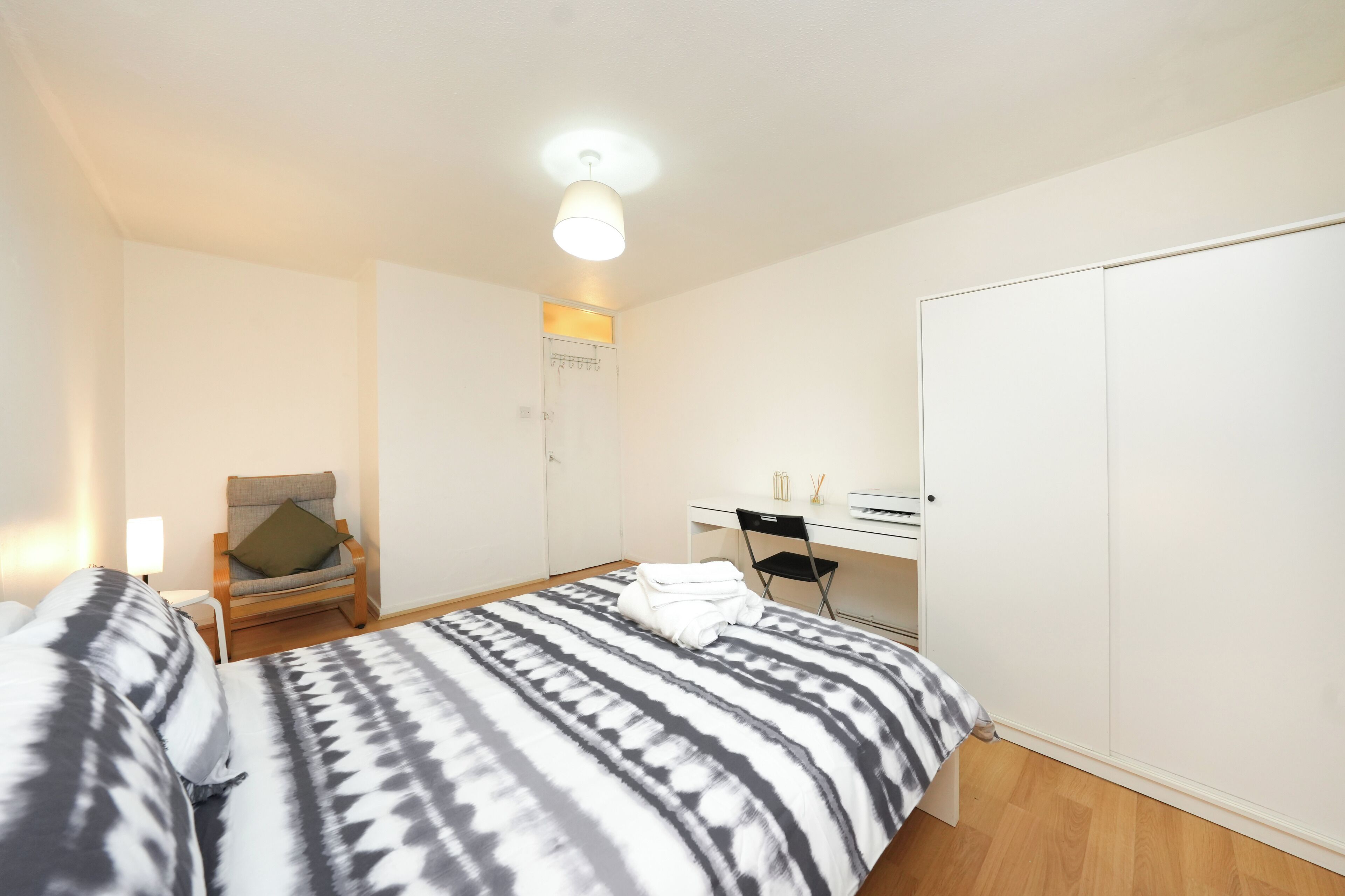 A bedroom with a bed, a chair, a desk, and a wardrobe.