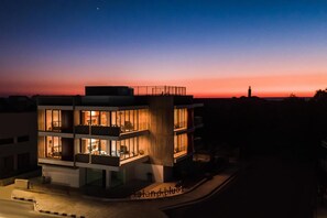 A multi-story building with illuminated interior spaces, a balcony, and a clear view of the surrounding area at dusk.