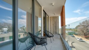 A balcony with two black wire chairs, a glass door, and a view of a road and greenery. - Avenue 202 1 BED - One Bedroom Apartment, Sleeps 2 (Pafos)
