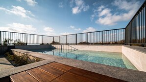 A rooftop pool with a wooden deck, surrounded by a metal railing, and a clear sky in the background. - Avenue 202 1 BED - One Bedroom Apartment, Sleeps 2 (Pafos)