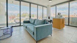 A modern living room with a sofa, a small table, and a cabinet. Large windows offer a view of the cityscape.