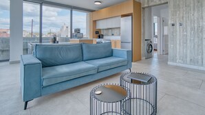 A modern living room with a blue sofa, two round tables, and a city view through large windows.