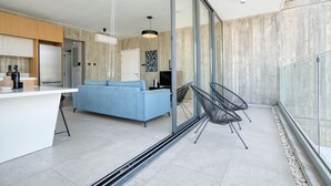 A modern kitchen with a white countertop, a blue sofa, and a glass door leading to a balcony with chairs.