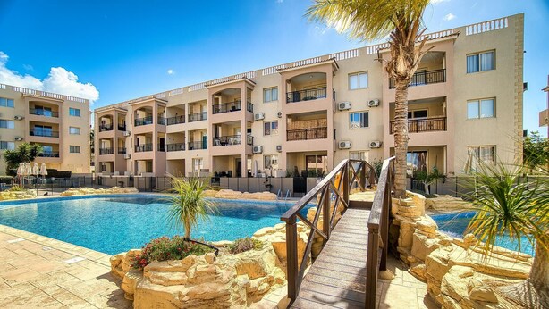 Un hotel su più piani con piscina, area salotto esterna e palme.