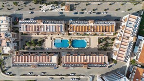 Ett flygbildsfoto av ett hotell med flera byggnader, en central pool och en parkeringsplats.
