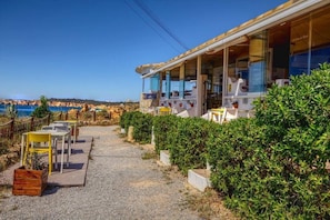 Una proprietà costiera con un'area salotto esterna coperta, un vialetto in ghiaia e vista sul mare.