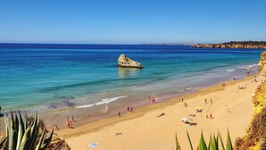A beach with clear blue water, a rocky outcrop, and people sunbathing. - Vacation Apartment In Portimao (Portimão)