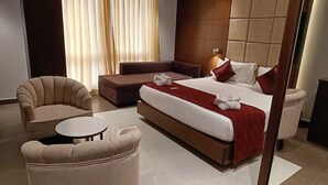 A modern hotel room with a large bed, a sofa, a round table, and a chair. - Hotel Darwin City  (Port Blair)