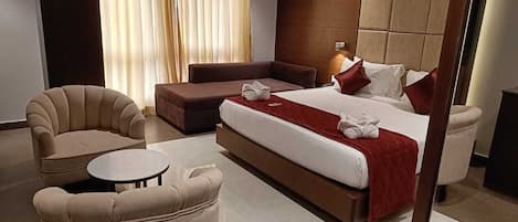 A modern hotel room with a large bed, a sofa, a round table, and a chair.