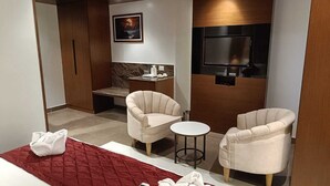 A hotel room with a bed, two armchairs, a small table, a TV mounted on the wall, and a painting above the TV. - Hotel Darwin City  (Port Blair)