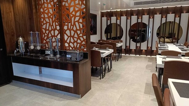 A modern restaurant interior with a central bar area, multiple dining tables, and a decorative wall with circular mirrors. - Hotel Darwin City  (Port Blair)