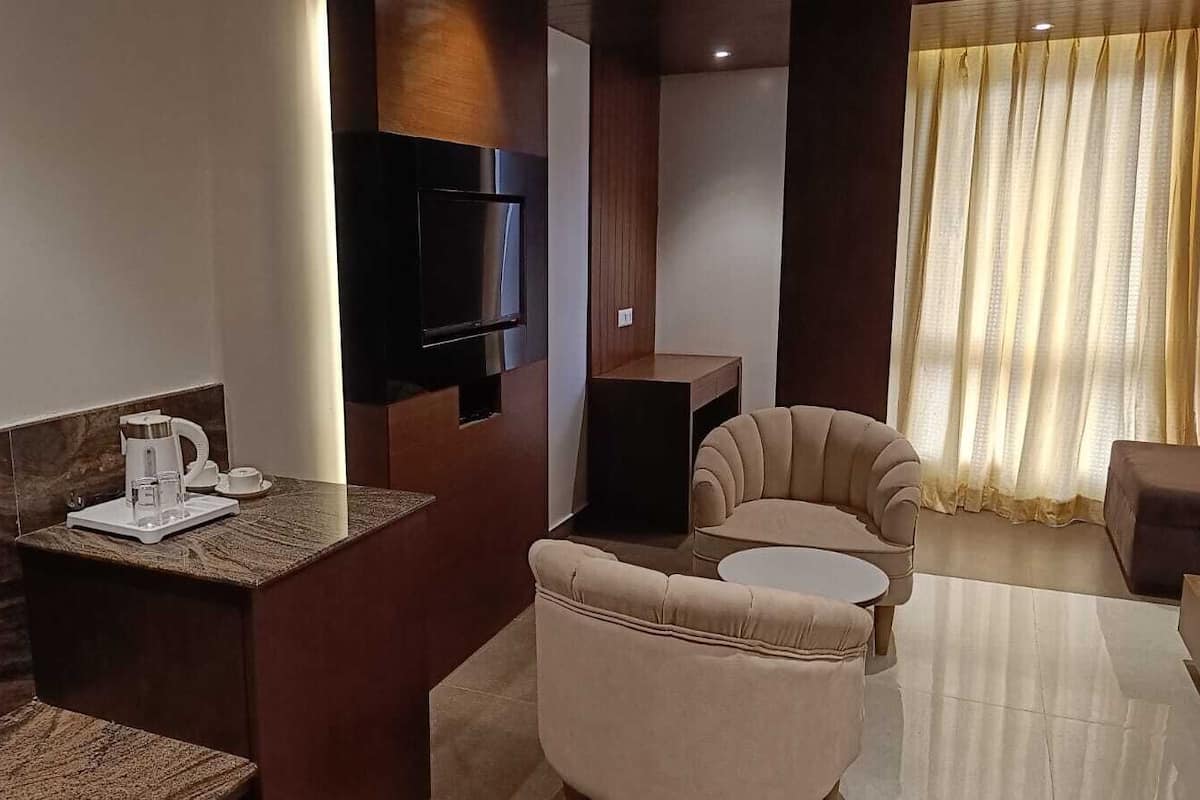 Quarto de hotel moderno com televisão de tela plana, espaço para café, sofá e área de refeições.