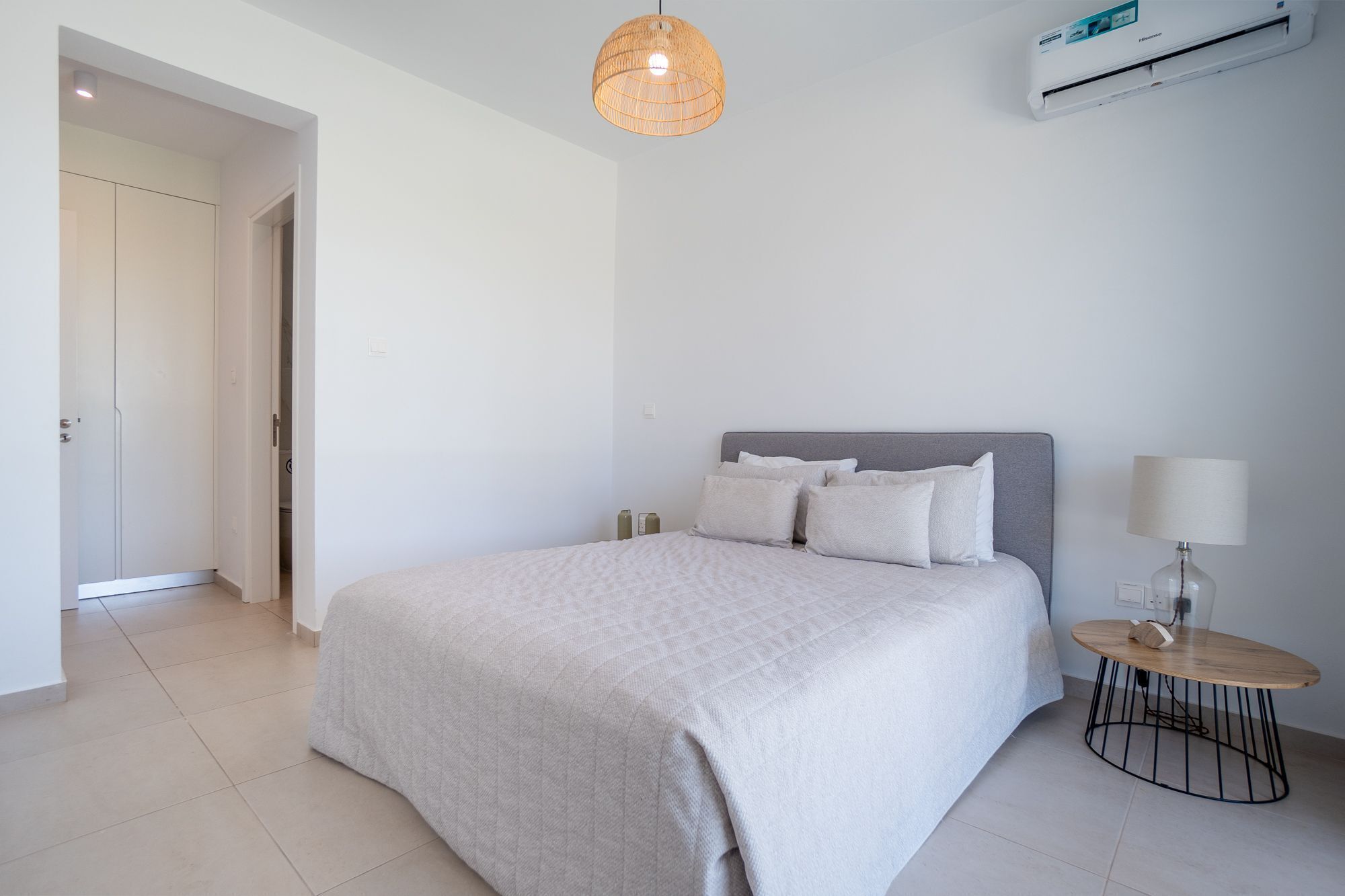A bedroom with a bed, bedside table, lamp, and an air conditioning unit.