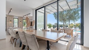 Ein moderner Essbereich mit einem großen Tisch und Stühlen, einer Ziegelwand und großen Fenstern mit Blick auf einen Pool und einen Garten.