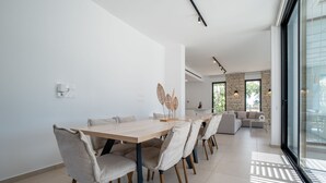Ein moderner Essbereich mit einem Holztisch und -stühlen, einer Zierpflanze und Blick auf das Wohnzimmer mit einer Couch und einem Couchtisch.
