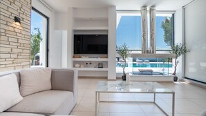Ein modernes Wohnzimmer mit einer Couch, einem Flachbildfernseher, einem Glastisch und Blick auf Pool und Außenbereich.