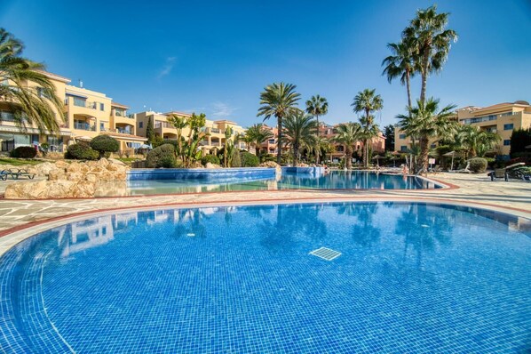 Una piscina grande y cristalina rodeada de palmeras y edificios de hotel.