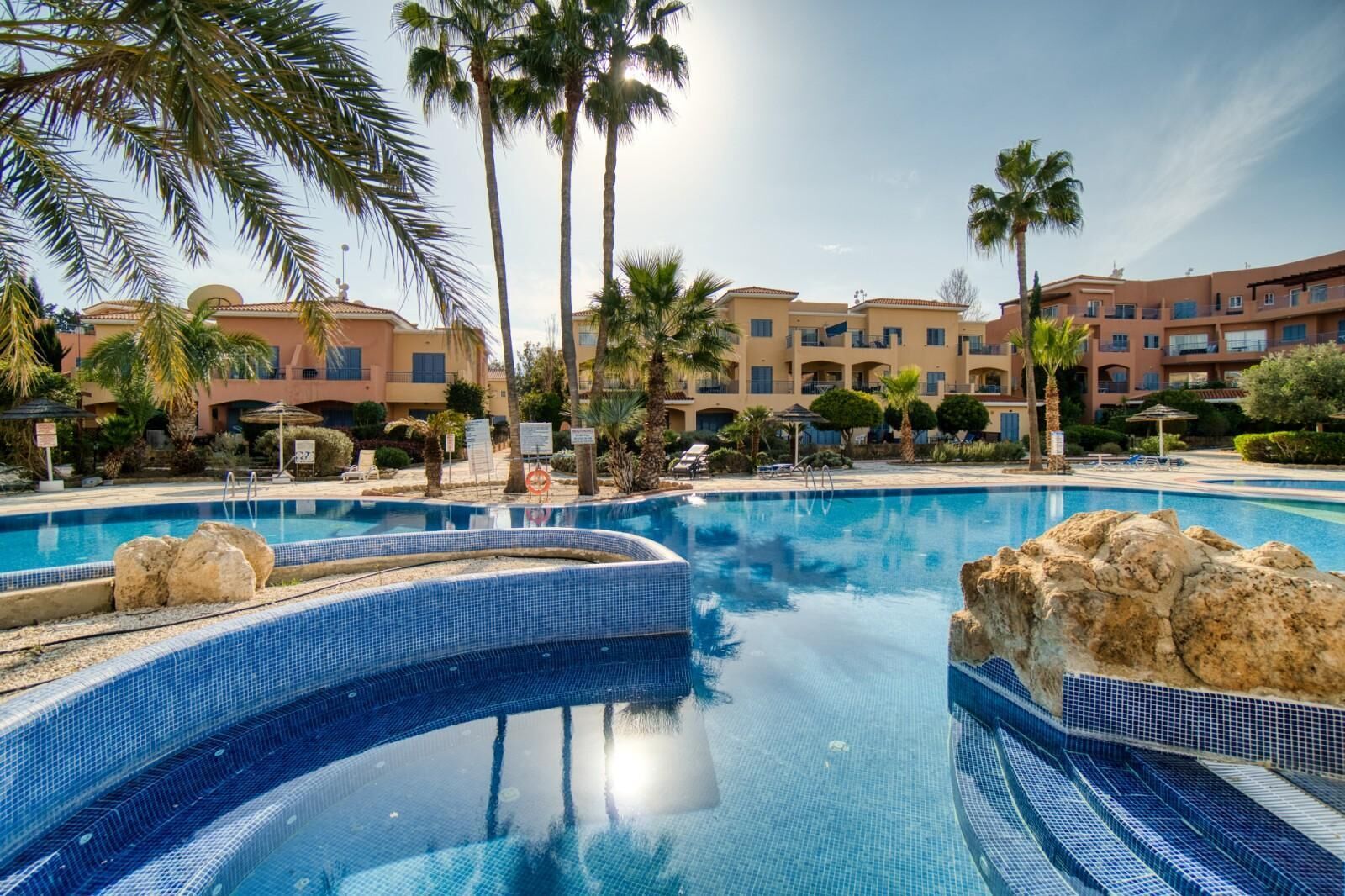 Une piscine à l’eau d’un bleu cristallin, entourée de palmiers et avec un bâtiment d’hôtel en arrière-plan.