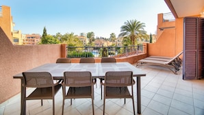 Un balcon avec une table et des chaises, une piscine en arrière-plan et des bâtiments environnants.