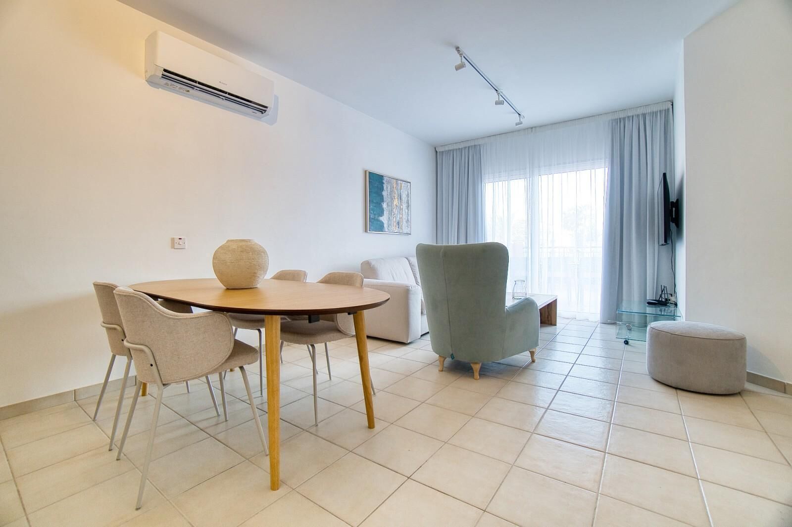 A modern living room with a round table, two armchairs, a sofa, and a TV.