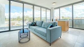 Un salon moderne avec un canapé bleu, une table basse ronde et une vue sur la ville grâce à de grandes fenêtres.