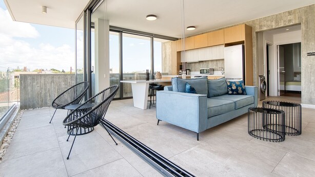 Un appartement moderne doté d’un balcon, d’un espace de vie avec un canapé et des fauteuils, d’une cuisine et offrant une vue sur la ville.