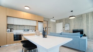 Une cuisine moderne avec un îlot central, des tabourets de bar et un canapé bleu dans l’espace salon.