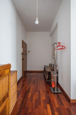 Un pasillo con suelo de madera, un aparador de madera, una puerta con un teléfono y un perchero con varios objetos.