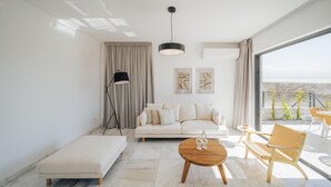 Een moderne woonkamer met een bank, een lange zitbank, een ronde houten salontafel en een rieten fauteuil.