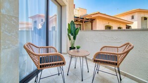En balkon med to fletstole, et lille bord, en potteplante og udsigt til omkringliggende bygninger.