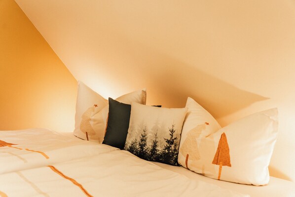 A bedroom with a sloped ceiling, a bed with white bedding, and several pillows with nature-themed designs. - Haus Abendrot (Sayda)