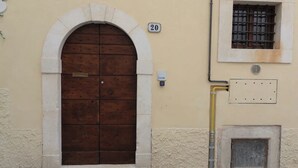 A building with a large wooden door, a small window with bars, and a number '20' sign.