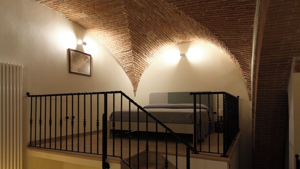 A bedroom with a brick ceiling, a staircase with a black railing, and a bed with a gray headboard.