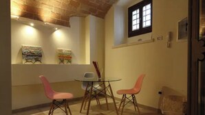 A dining area with a round table and three chairs, a brick wall, and artwork on the wall.