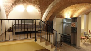 A bedroom with a bed, a staircase, and a kitchenette area.