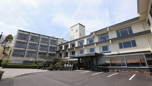 A multi-story hotel with a modern design, featuring a central entrance, a clock tower, and a parking area with a gravel driveway. - Miyahama Grand Hotel (Hatsukaichi)