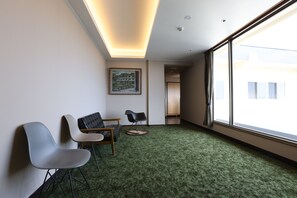 A room with a green carpet, two modern chairs, a sofa, a painting on the wall, and a large window with curtains. - Miyahama Grand Hotel (Hatsukaichi)