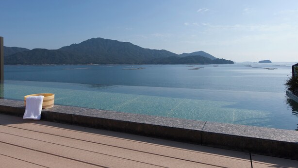 A clear view of a swimming pool with a towel and a wooden bucket on the edge, overlooking a calm sea and distant mountains. - Miyahama Grand Hotel (Hatsukaichi)