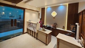 A reception area with a marble counter, a receptionist, and a decorative wall piece. - Shree Shivya Namahstubhyam Hotel (Varanasi)