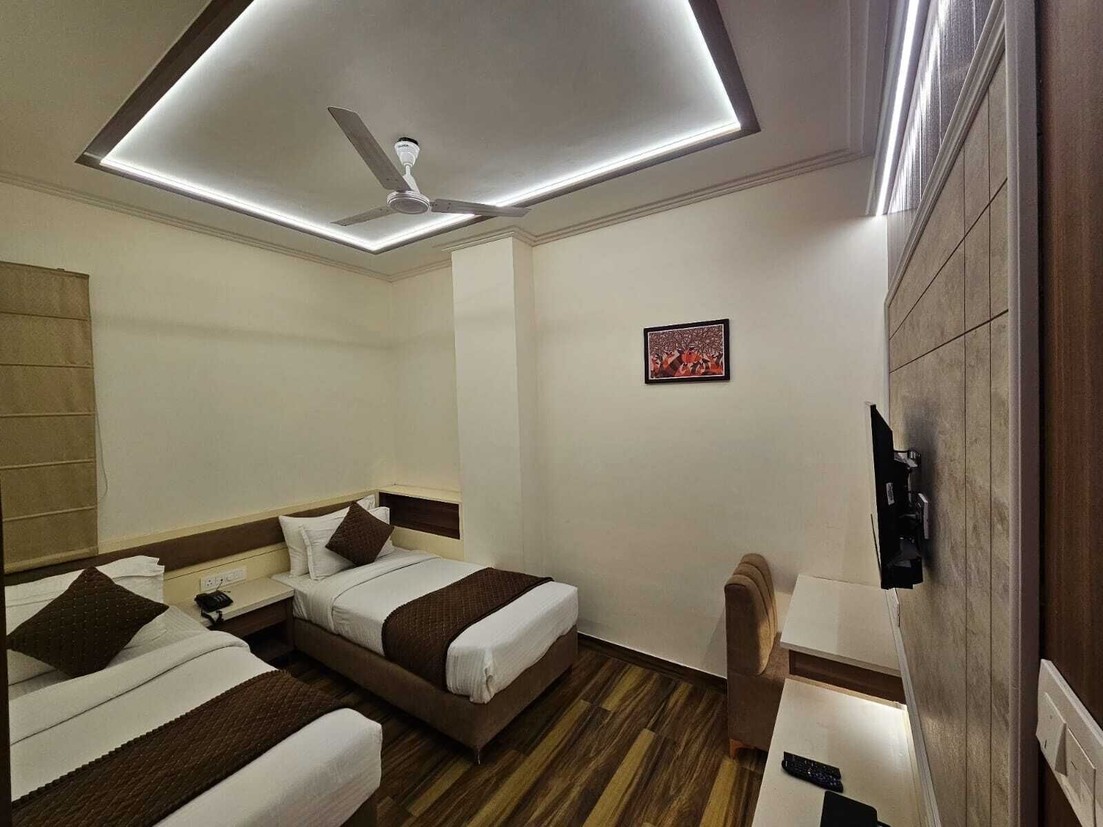 A hotel room with two beds, a ceiling fan, a small table, and a wall-mounted TV.