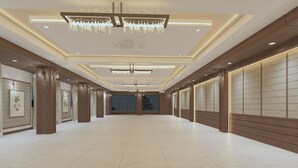 A spacious hotel lobby with a high ceiling, chandeliers, wooden paneling, and a tiled floor. - Shree Shivya Namahstubhyam Hotel (Varanasi)