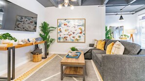 A modern living room with a grey sofa, wooden coffee table, and a large abstract painting on the wall. - Gorgeous Villa Steps to La Jolla Cove (San Diego)