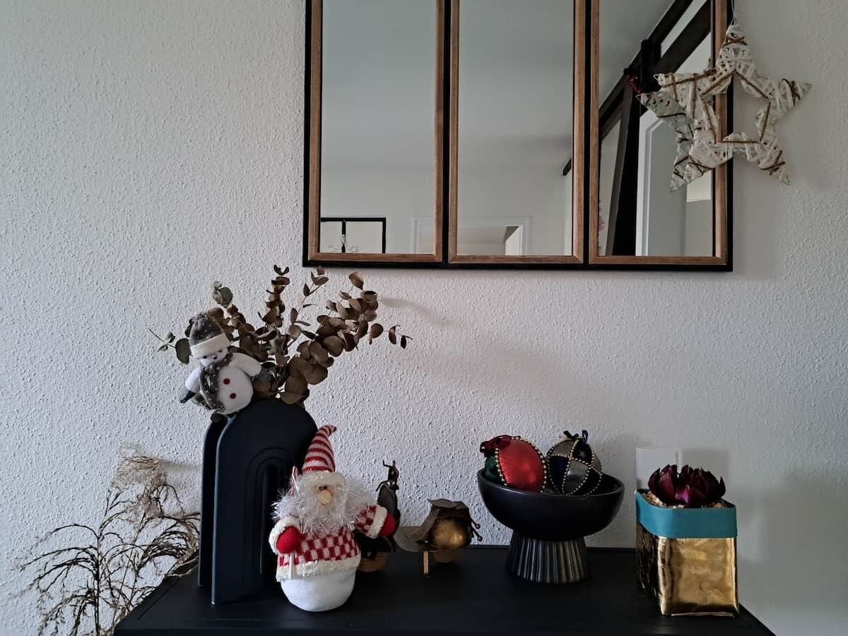 A room with a black table displaying various decorative items including a Santa Claus figurine, a vase with dried branches, and a bowl with ornaments.