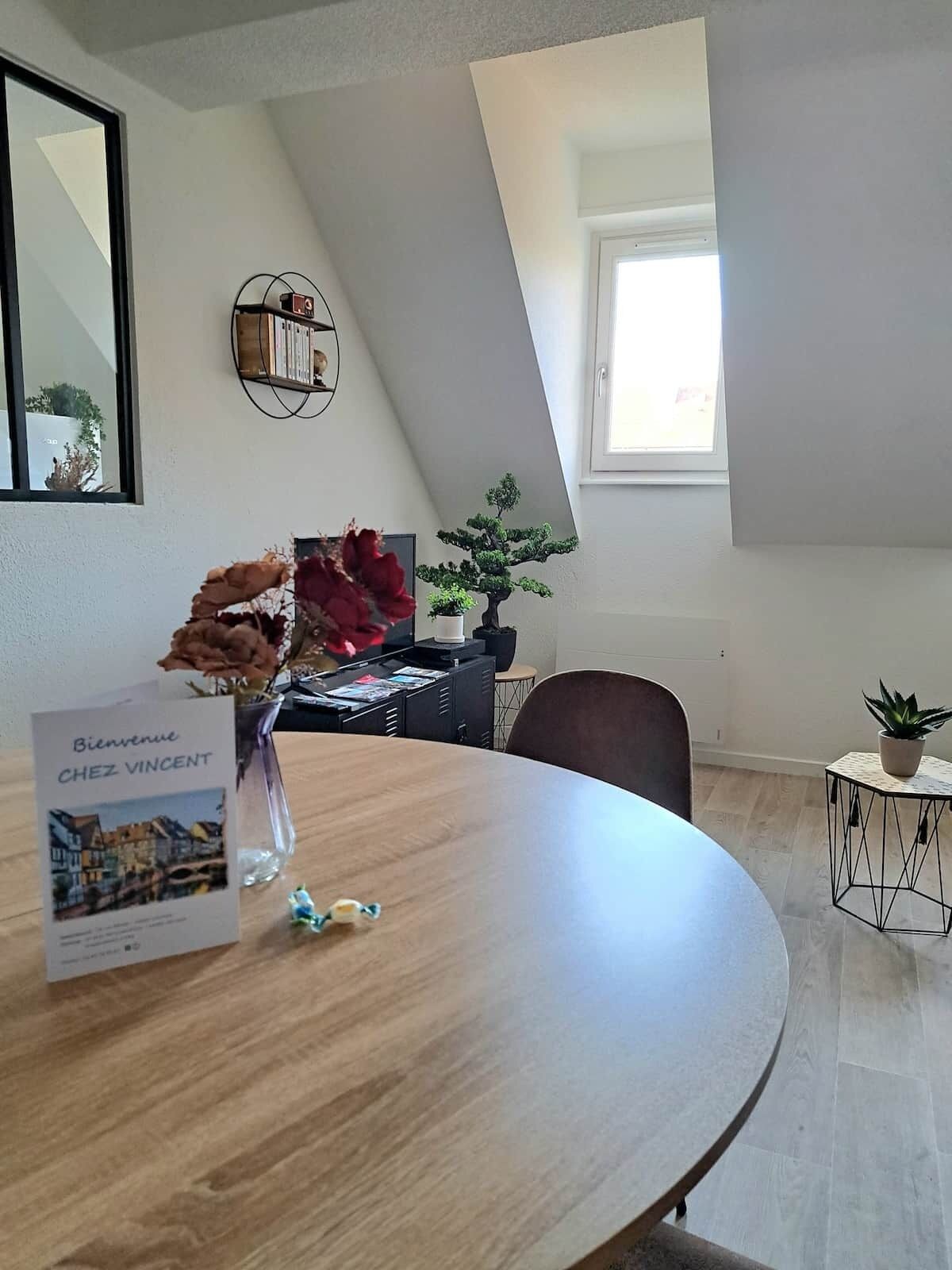 A modern interior with a round table, a bonsai tree, and a welcome sign.