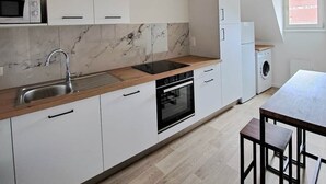 Una cuina moderna amb armaris blancs, taulell de fusta, forn integrat, microones i rentadora.