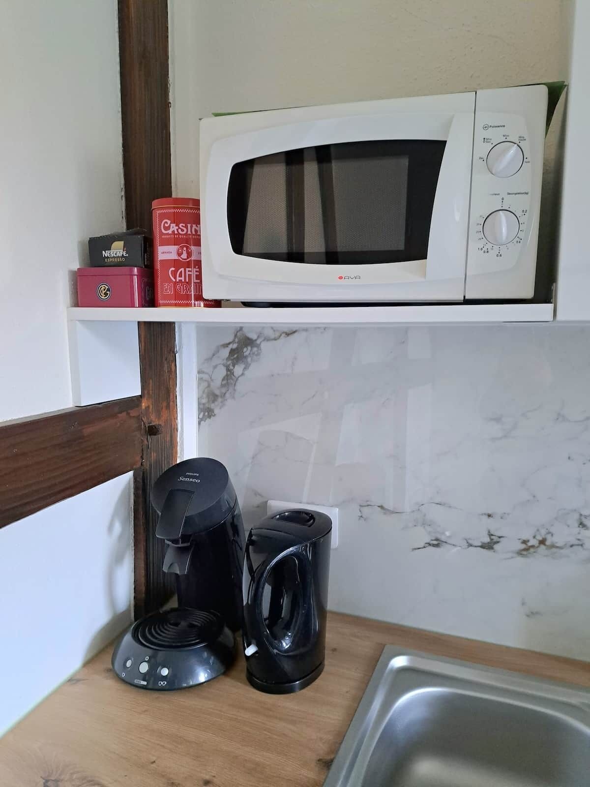 Une cuisine équipée d’un four à micro-ondes posé sur une étagère, d’une machine à café et d’une cafetière sur le plan de travail.