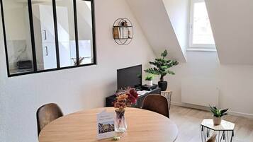 A modern dining area with a round table, four chairs, a ceiling fan, a large mirror, and a potted plant.
