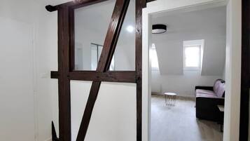 An interior space with a wooden ceiling beam structure, a modern light fixture, and a view into a living area with a sofa.