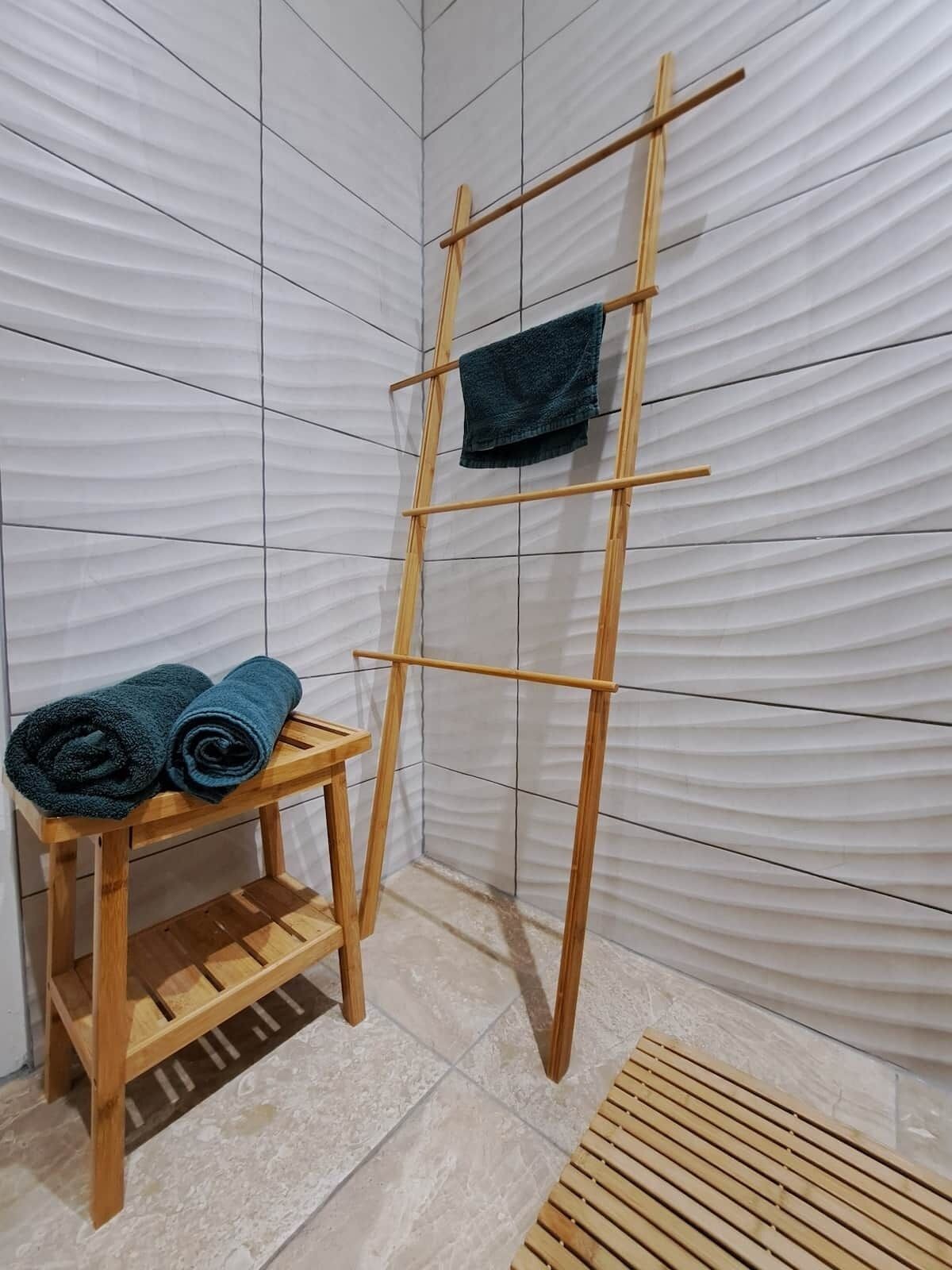 A wooden drying rack with towels, a wooden stool, and a tiled wall.