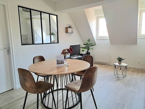 A modern dining area with a round table and six chairs, a large mirror, and a small side table with a plant.